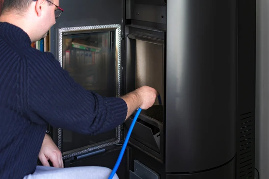 Technicien qualifié en tenue de travail professionnelle effectuant un diagnostic de dépannage sur un poêle à granulés défaillant en environnement résidentiel. Le technicien utilise un instrument de diagnostic ou un outil de vérification tout en inspectant le système de combustion ou les éléments internes du poêle. La scène montre clairement une intervention de maintenance corrective, avec l'appareil partiellement ouvert ou inspecté, et le technicien concentré sur son diagnostic.